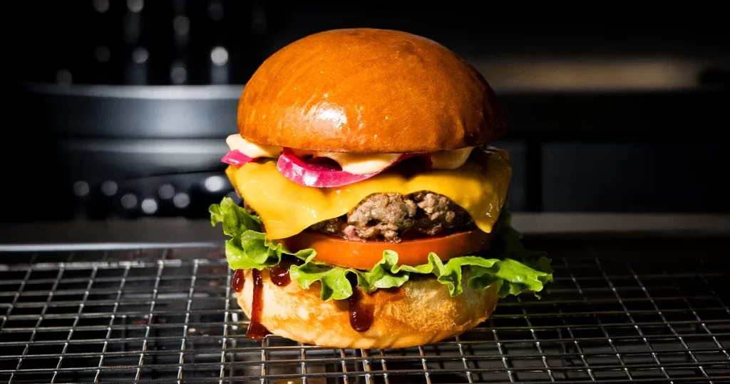 A juicy Fat Bull Co. burger with a hand-pressed beef patty, melted cheese, pickled red onion, lettuce and tomato on a toasted brioche bun, finished with a drizzle of sauce.